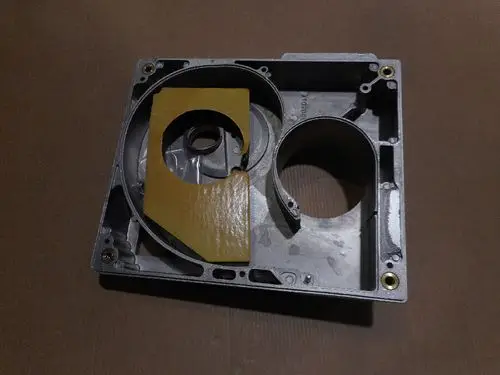 Gehäuse von Remeha mit Ausschnitten, einer runden Öffnung und einer flachen Fläche, die mit einem gelben Material bedeckt ist. Die Rückseite ist uneben mit Schraublöchern.